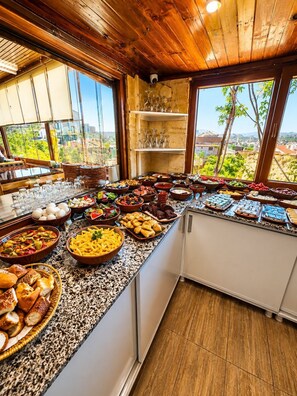 A buffet with various food items and a view of the outdoors through large windows. - Saklı Cave House (Avanos)