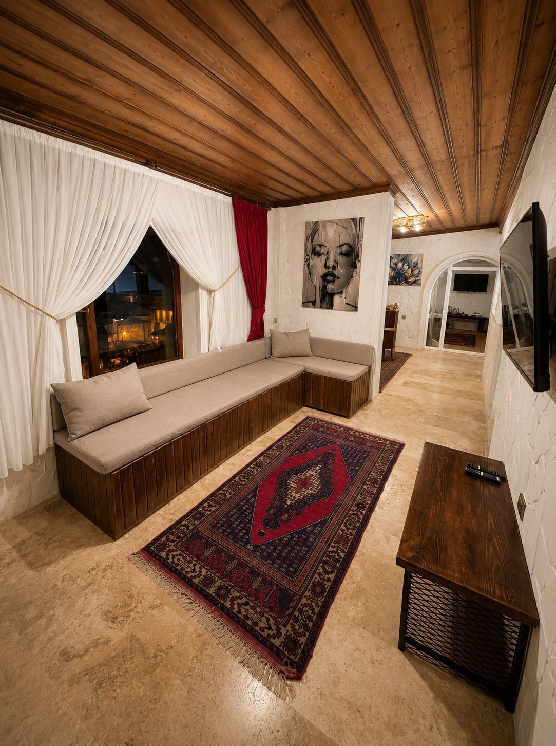 Un salon chaleureux avec un canapé d’angle, un tapis à motifs et un téléviseur fixé au mur.