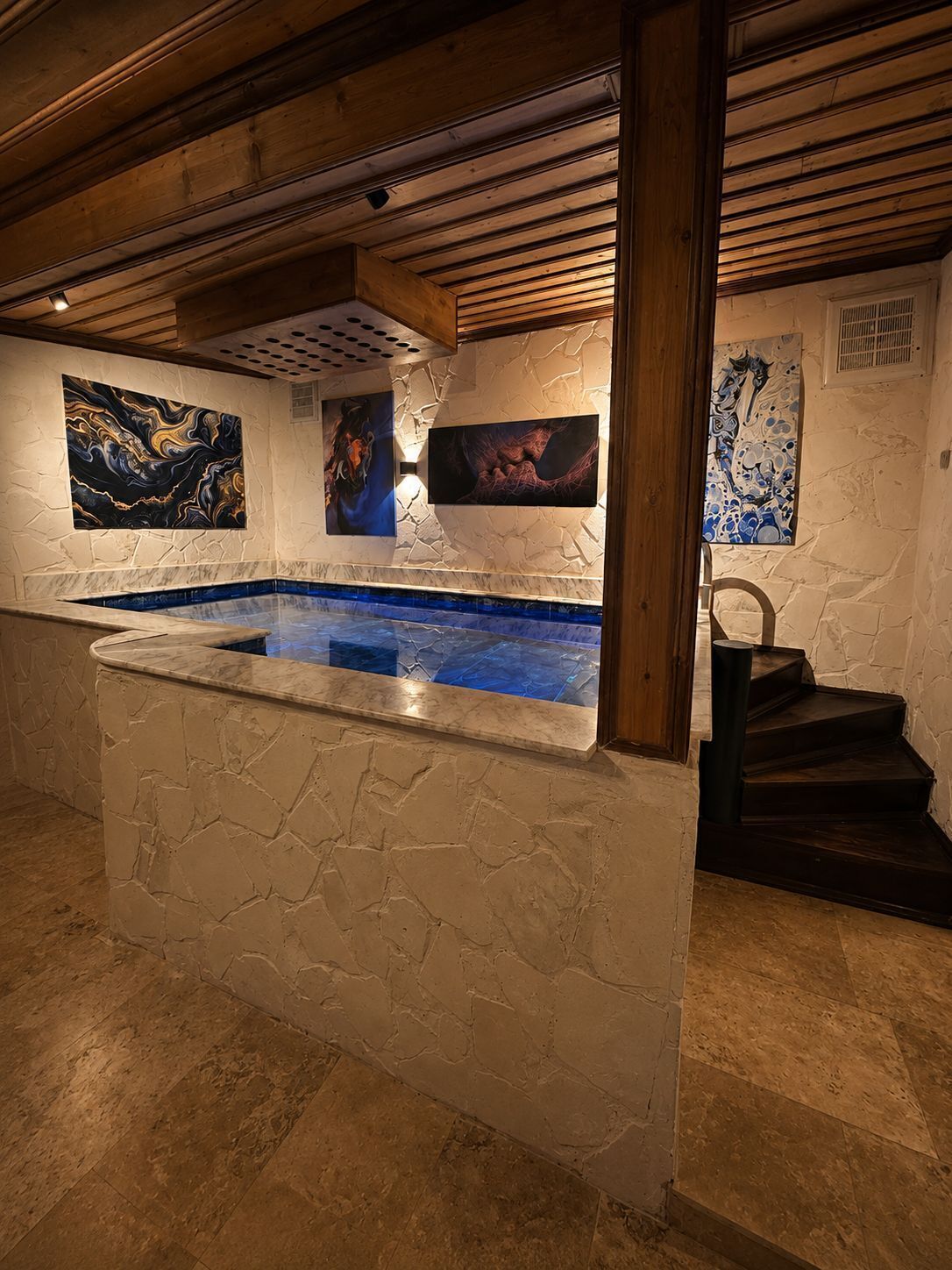 Un área de spa con pared de piedra, piscina de mármol y obras de arte en las paredes.