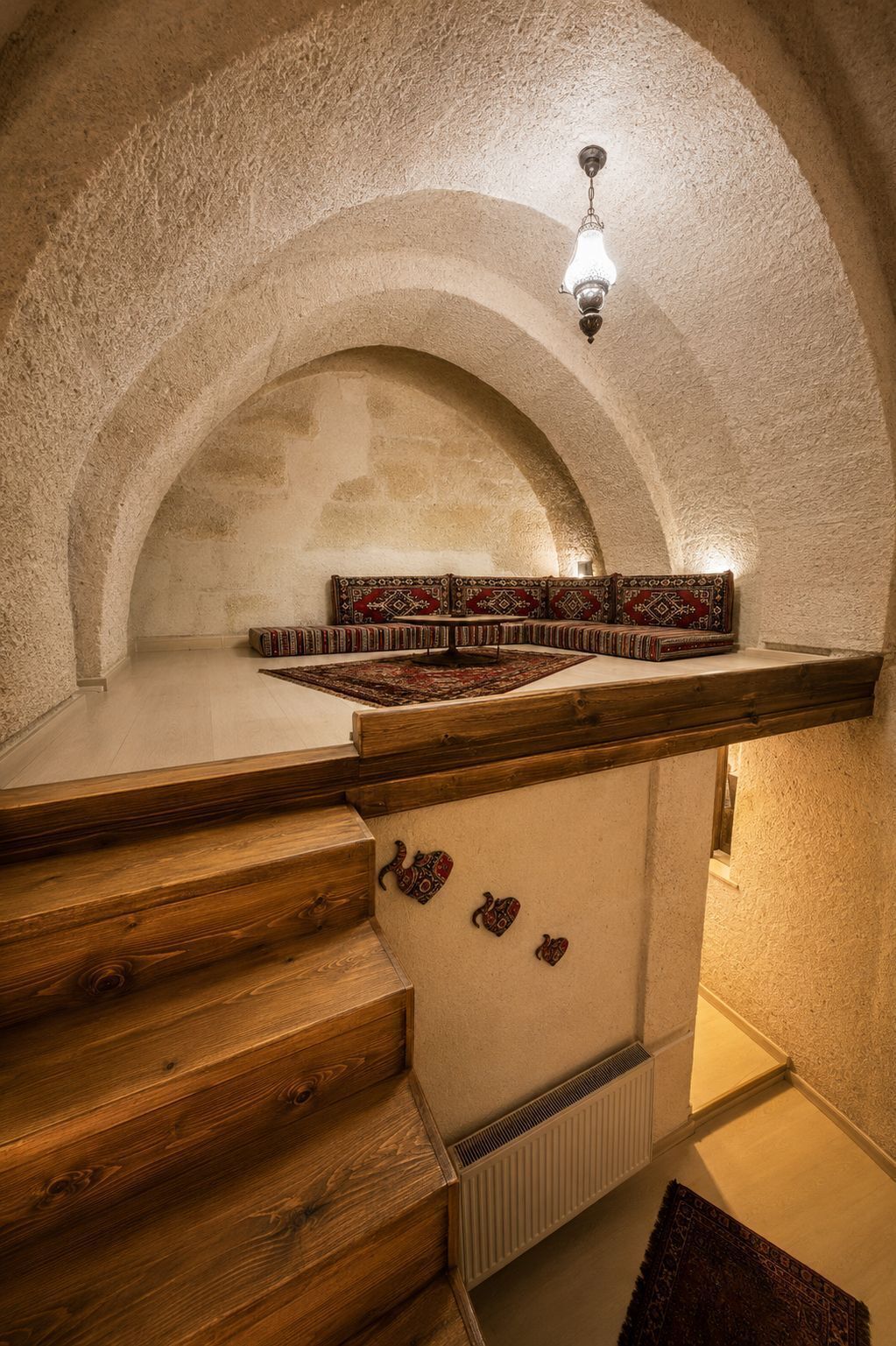 A room with arched ceilings, a wooden bench, a radiator, and a hanging light fixture.