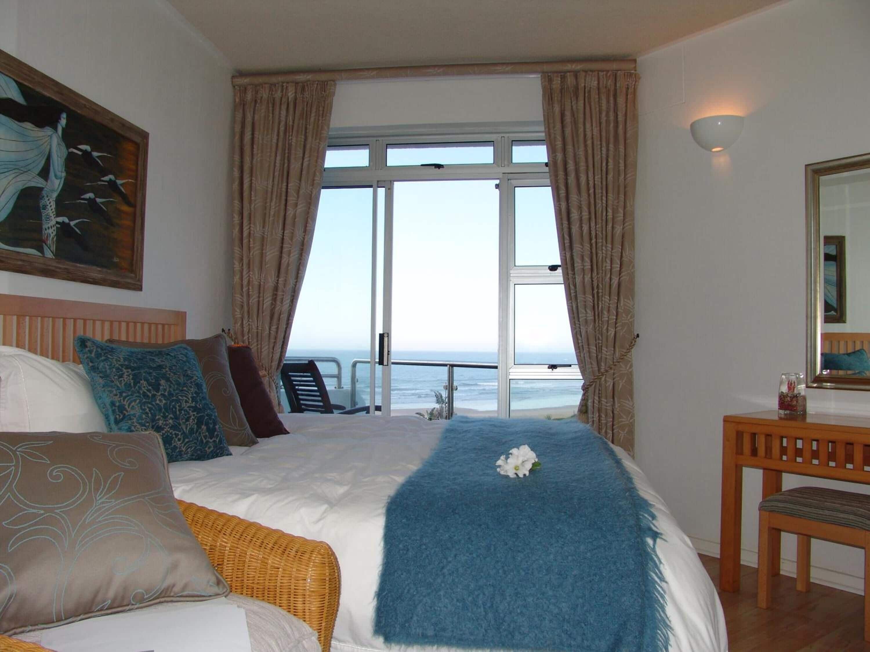 Habitación de hotel con una cama grande, vista al mar, un cuadro en la pared y una silla de madera.