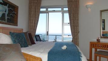 Habitación de hotel con una cama grande, vista al mar, un cuadro en la pared y una silla de madera.
