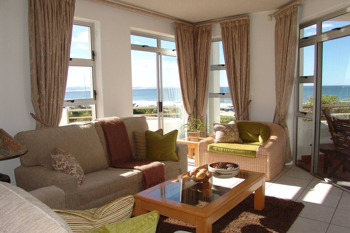 A living room with a sofa, armchairs, a coffee table, and a view of the sea through large windows.