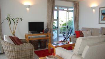 A living room with a television, wicker furniture, a red rug, and a balcony with a chair.