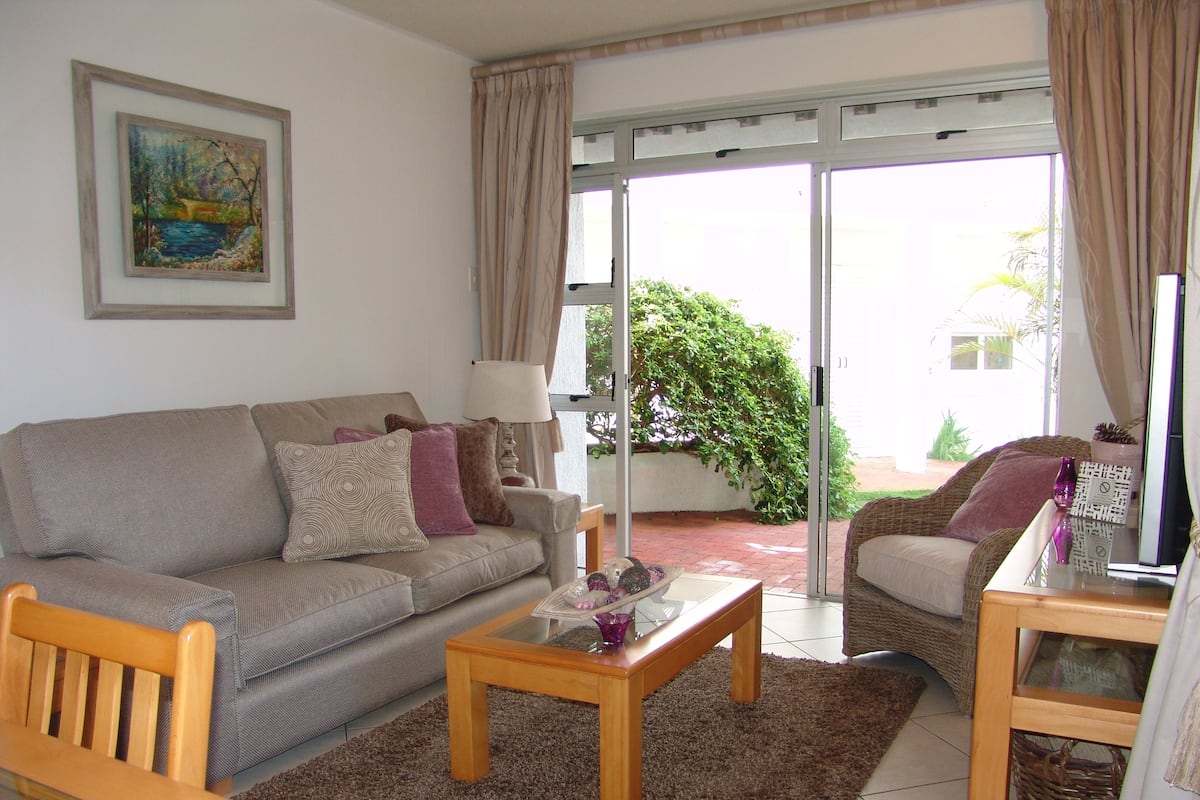 A living room with a sofa, armchair, coffee table, and a painting on the wall.