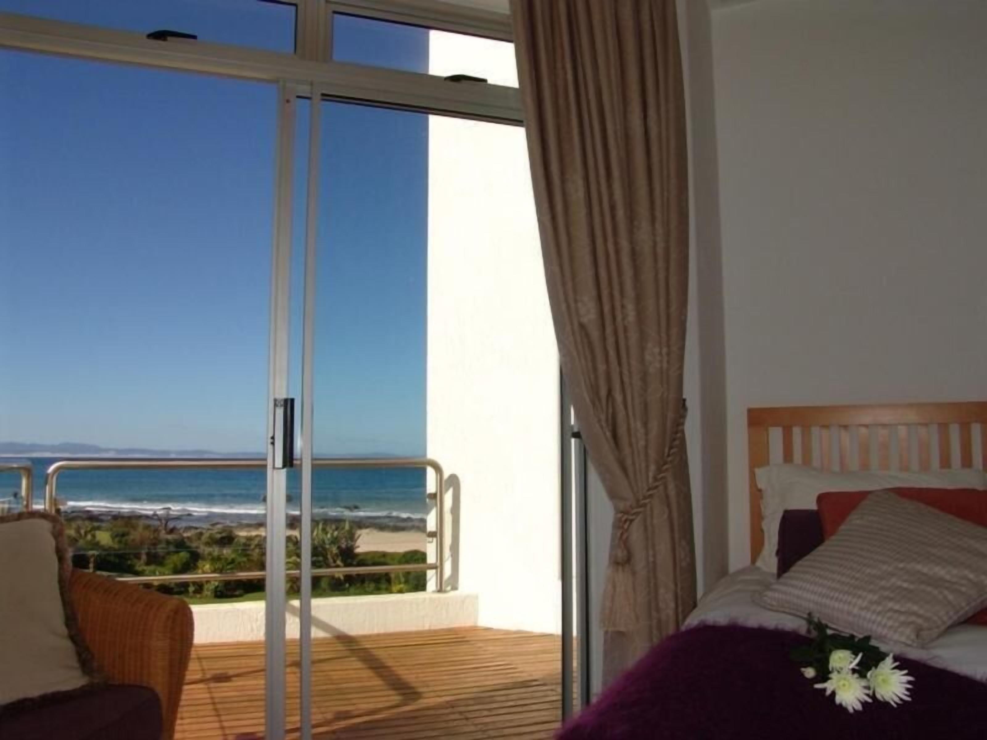 Un dormitorio con vista a la playa, un balcón con una silla y una cama con cabecera de madera.