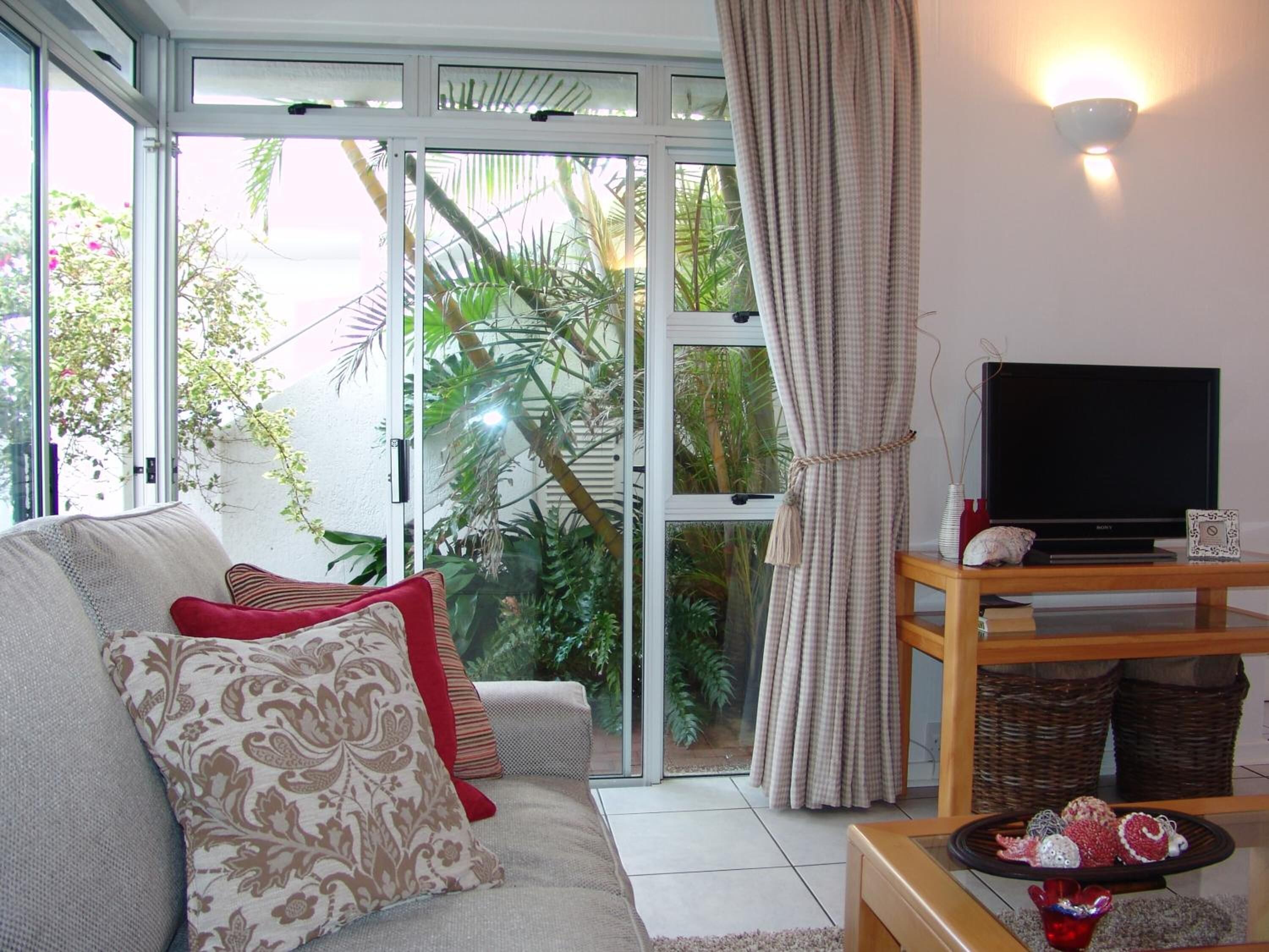 A living room with a sofa, television, and a view of greenery through a glass door.