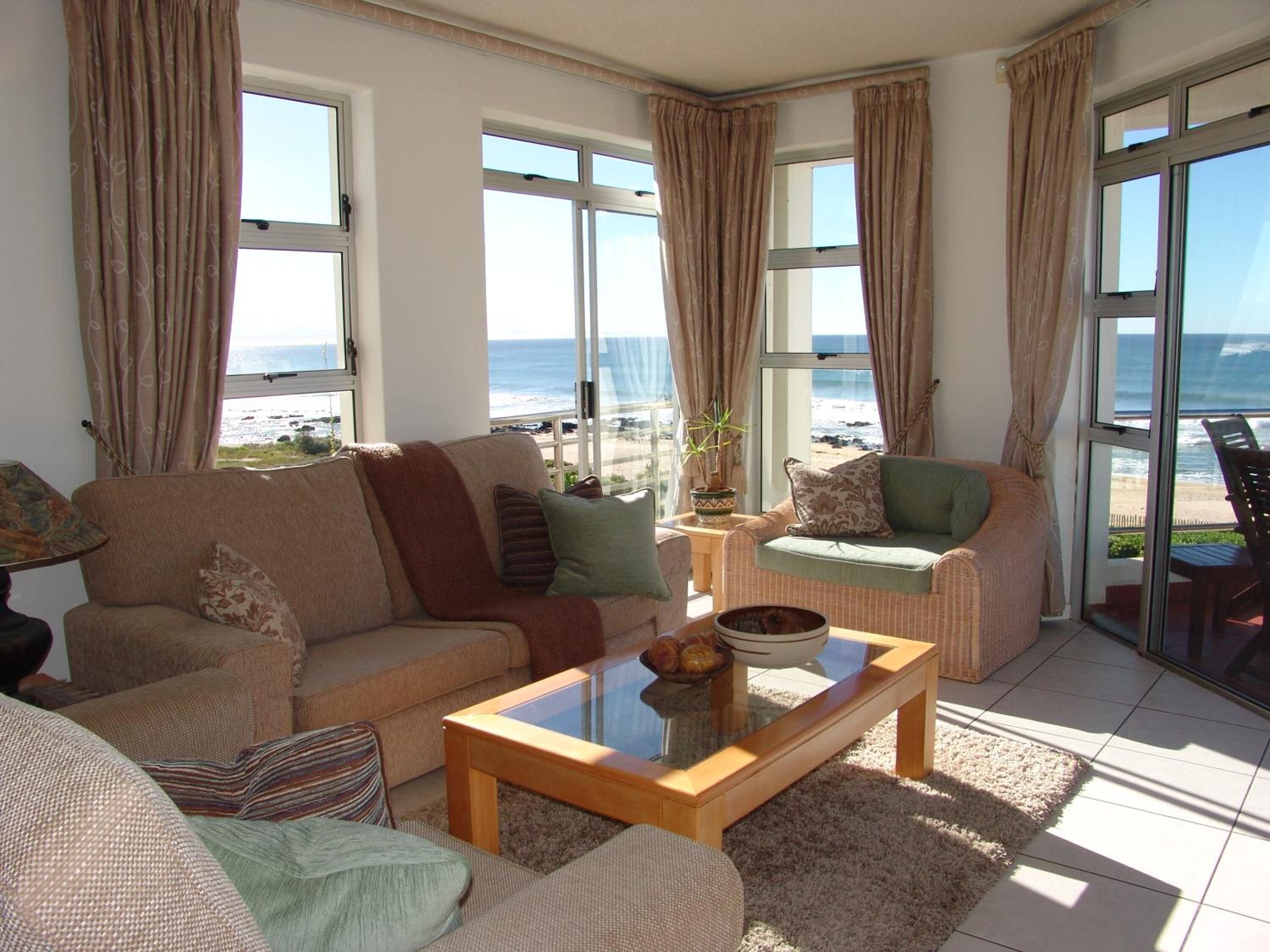 A living room with a sofa, armchairs, a coffee table, and a view of the beach.