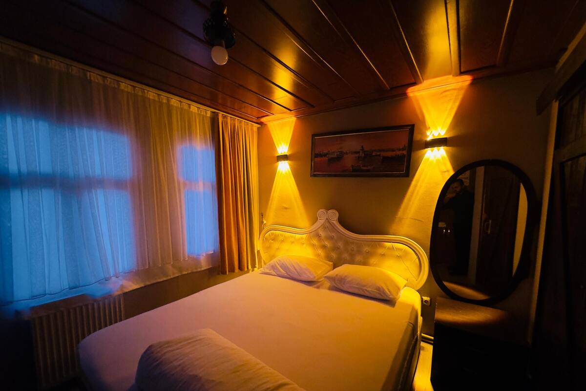A dimly lit hotel room with a large bed, a round mirror, and a painting on the wall.