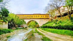 A stone bridge with a yellow building beneath it, surrounded by greenery and a dirt path. - Onuncu Koy Hotel - Adults Only (Bursa)