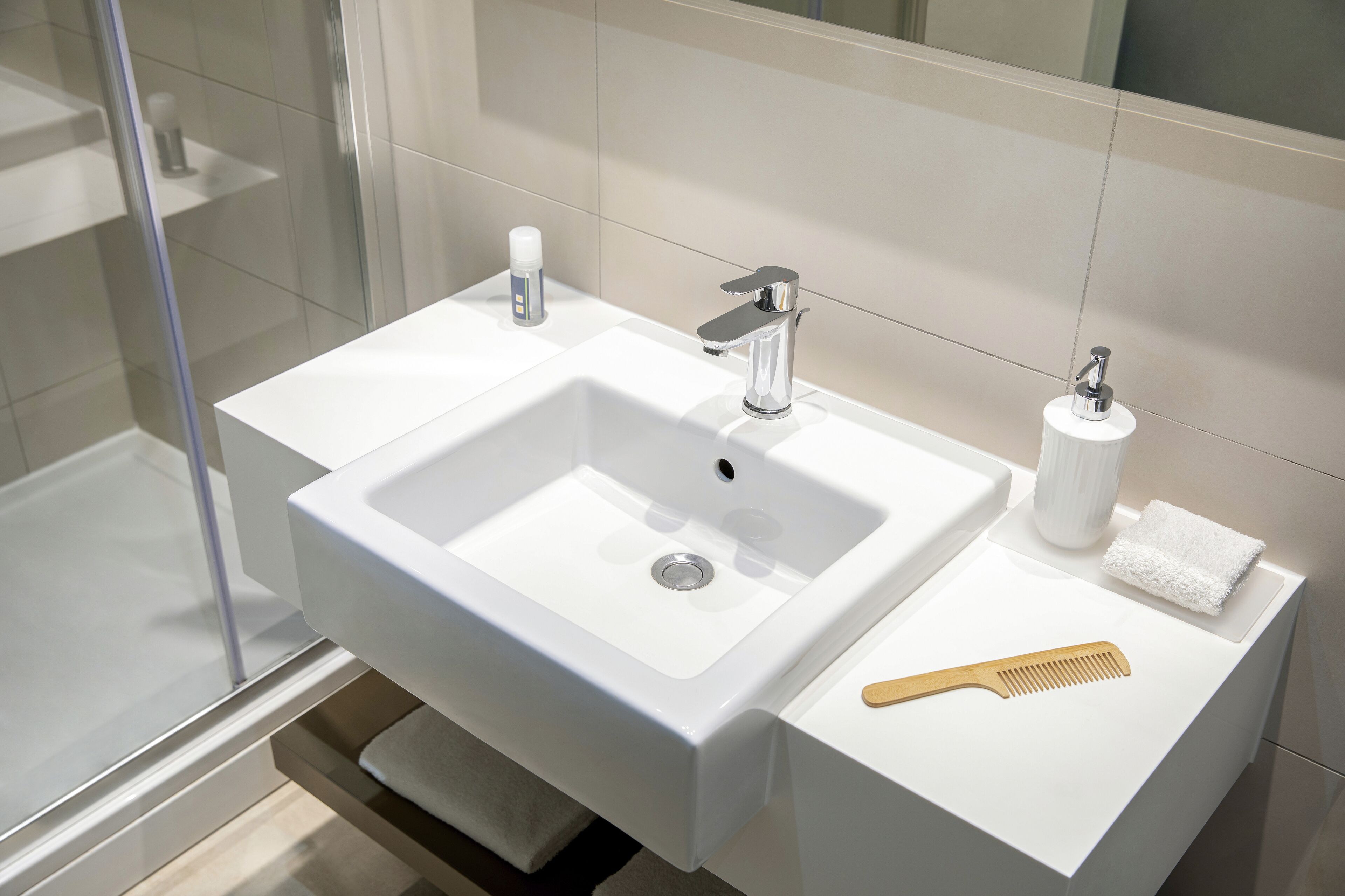 A modern bathroom with a white sink, chrome faucet, and a mirror above it.