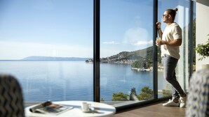 Una camera moderna con una grande finestra vista sulla costa, un tavolino con una tazza e una rivista.
