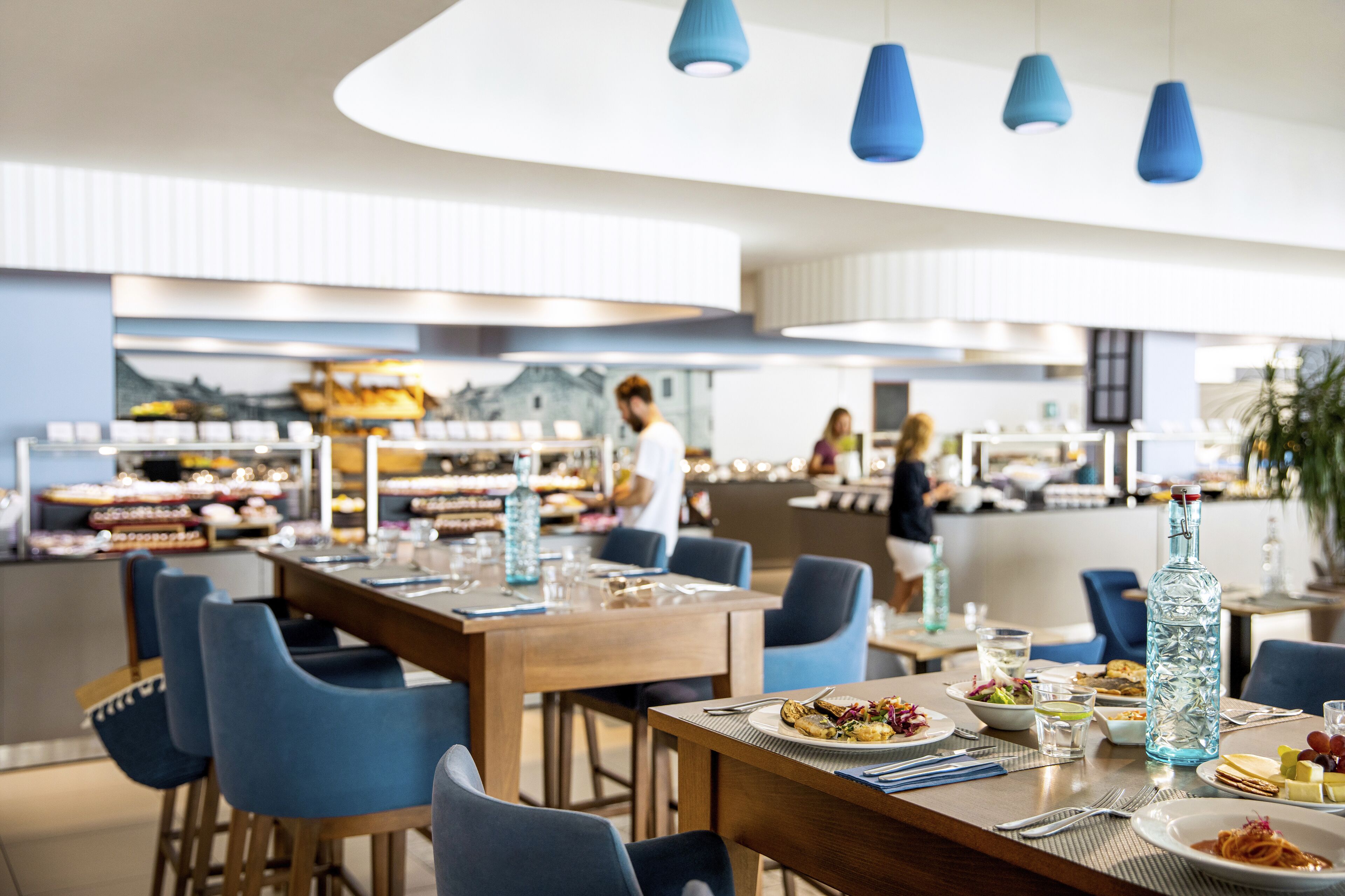 A modern dining area with blue chairs, wooden tables, and hanging blue pendant lights.