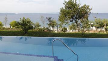A swimming pool with a metal ladder, surrounded by greenery and a view of the sea.
