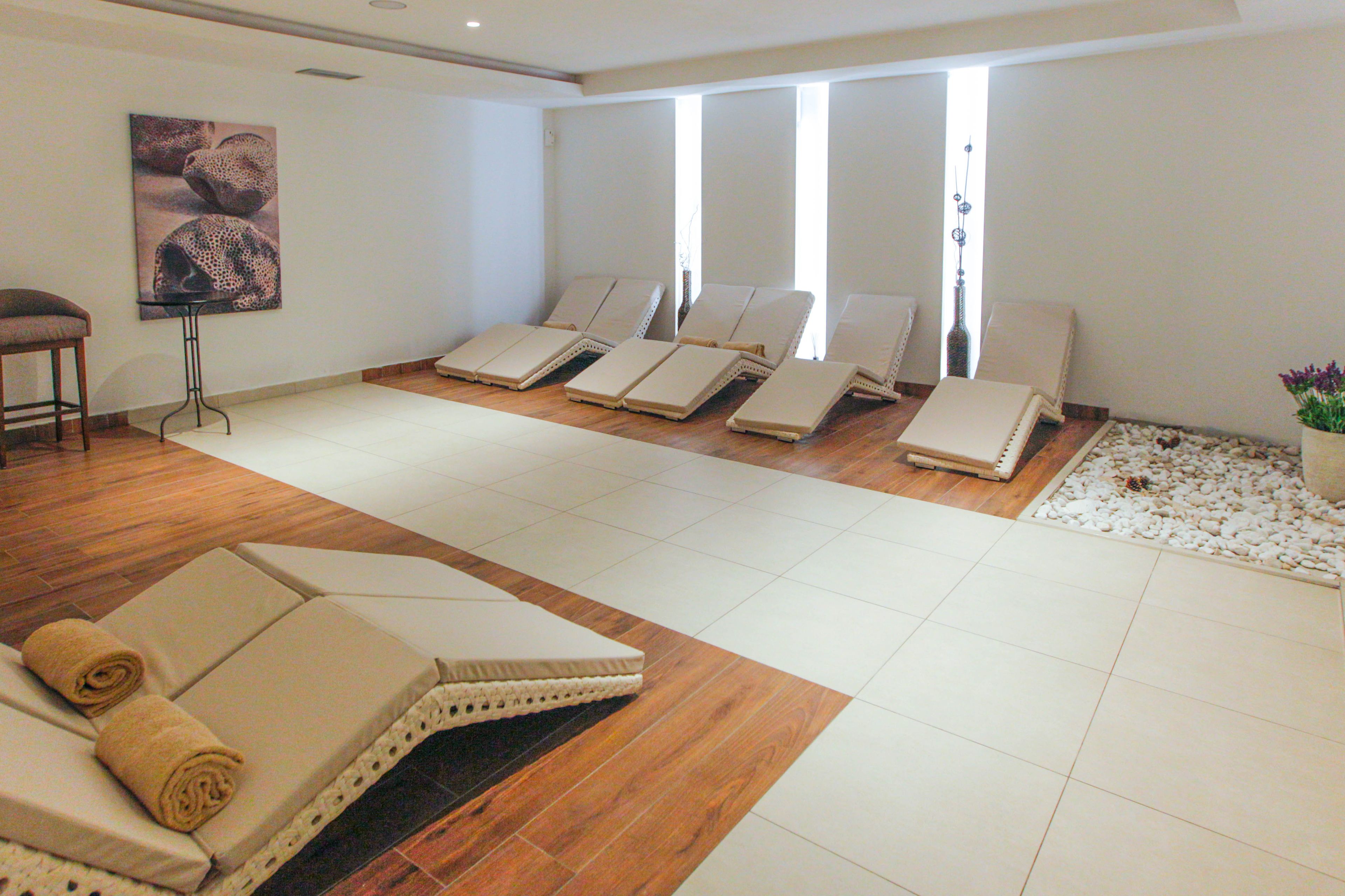 Une salle de spa équipée de plusieurs chaises longues, d’une table de massage et d’une grande fenêtre laissant entrer la lumière naturelle.