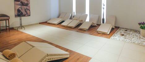 Une salle de spa équipée de plusieurs chaises longues, d’une table de massage et d’une grande fenêtre laissant entrer la lumière naturelle.