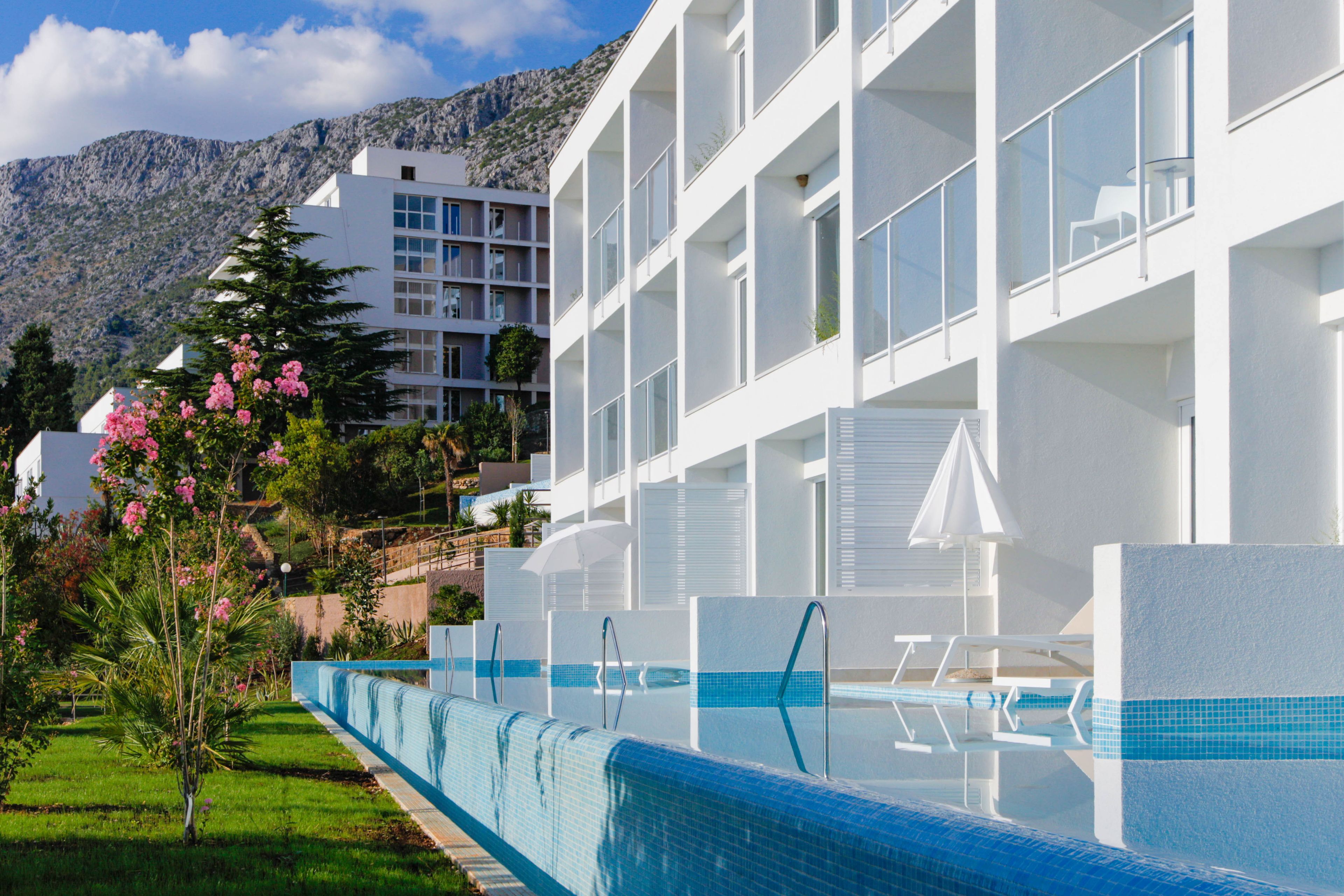 Un hotel moderno con piscina, balcones y montañas al fondo.