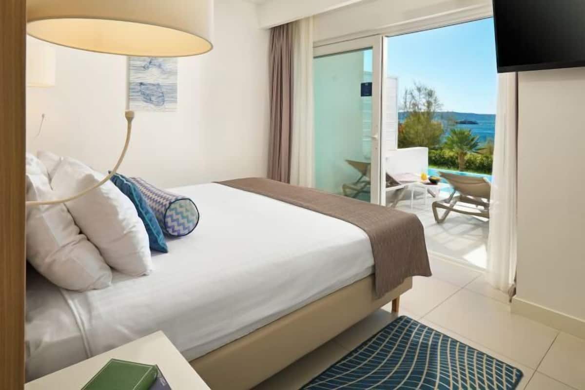 A hotel room with a bed, a TV, a balcony with a view of the sea, and a chair.