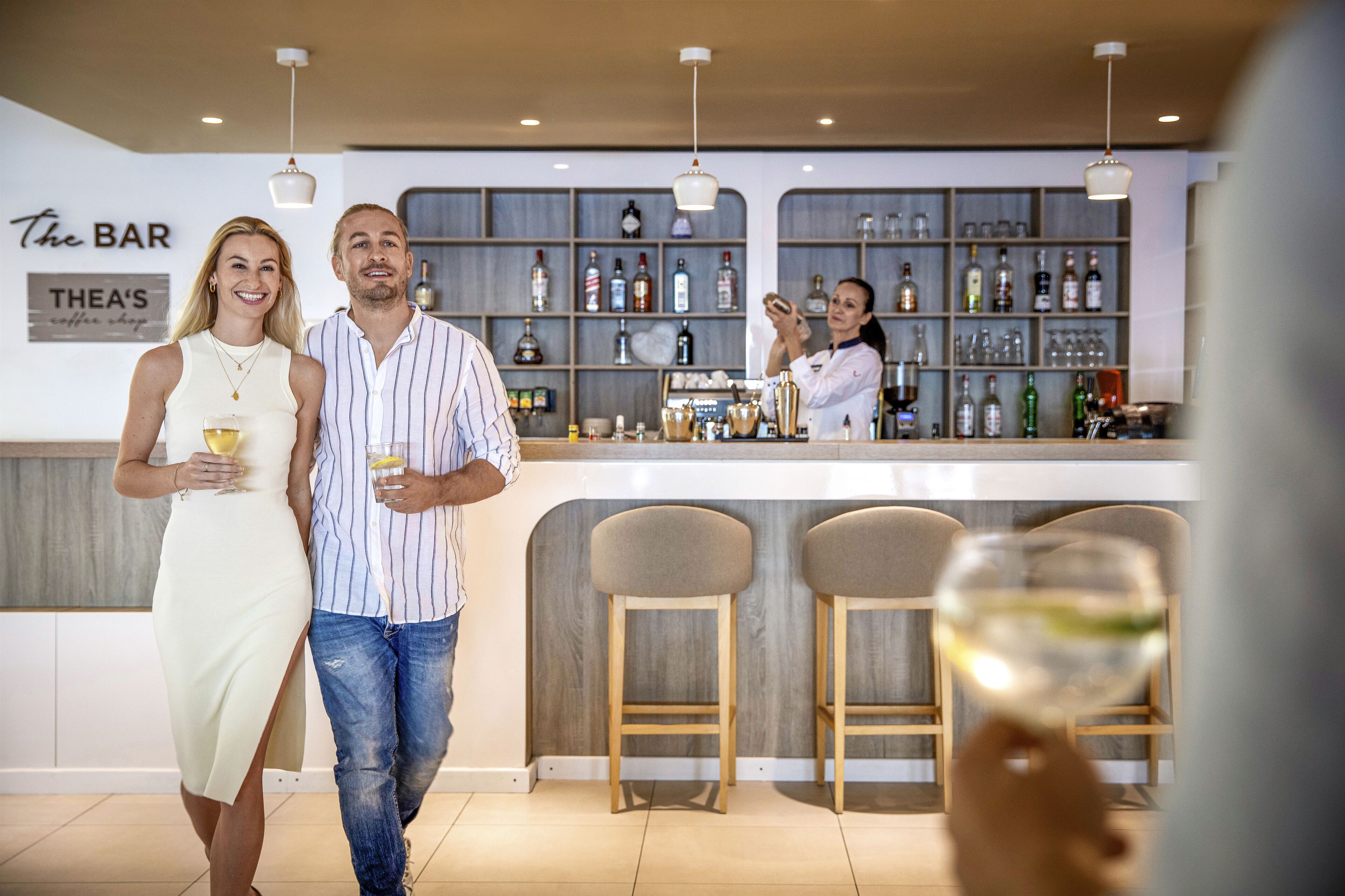 A bar area with a bartender, a couple, and bar stools.