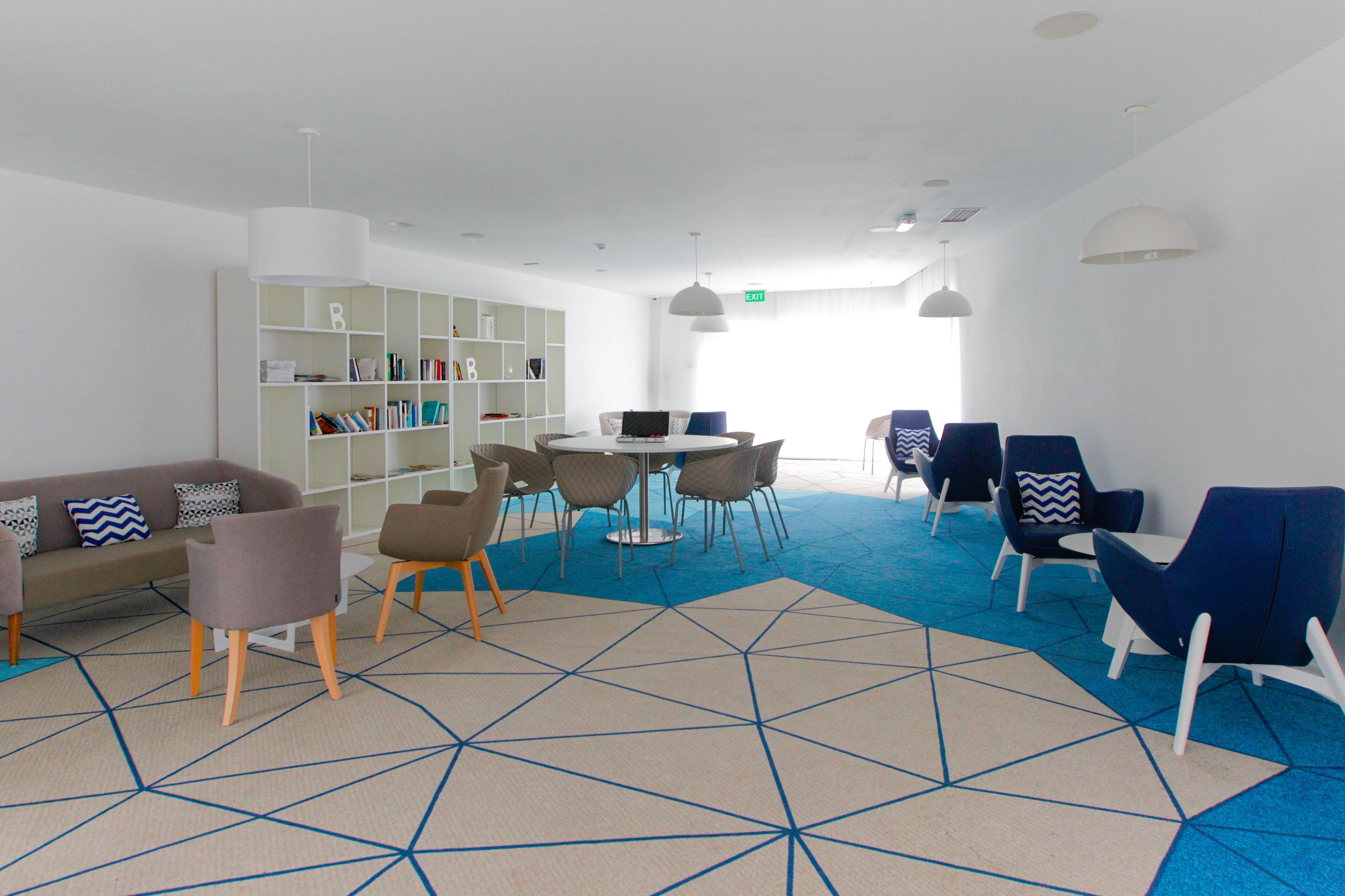 A modern lounge area with a sofa, chairs, a round table, and a bookshelf.