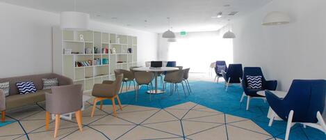 A modern lounge area with a sofa, chairs, a round table, and a bookshelf.