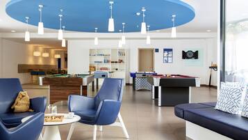 A modern living room with blue sofas, a pool table, and a billiards table. There are ceiling lights and a pool table in the background.