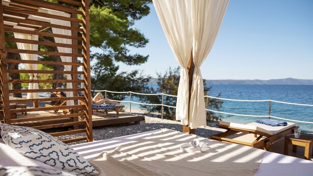 Una stanza fronte spiaggia con un letto, una sedia di legno e una poltrona prendisole vista mare.