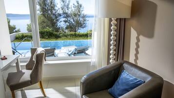 A room with a view of the sea, a dining area, and a seating area with a lamp.