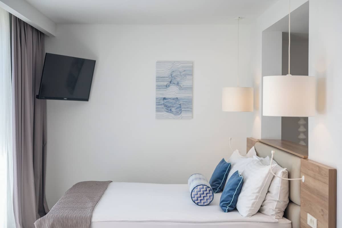 A hotel room with a bed, a flat-screen TV mounted on the wall, a bedside lamp, and a piece of wall art.