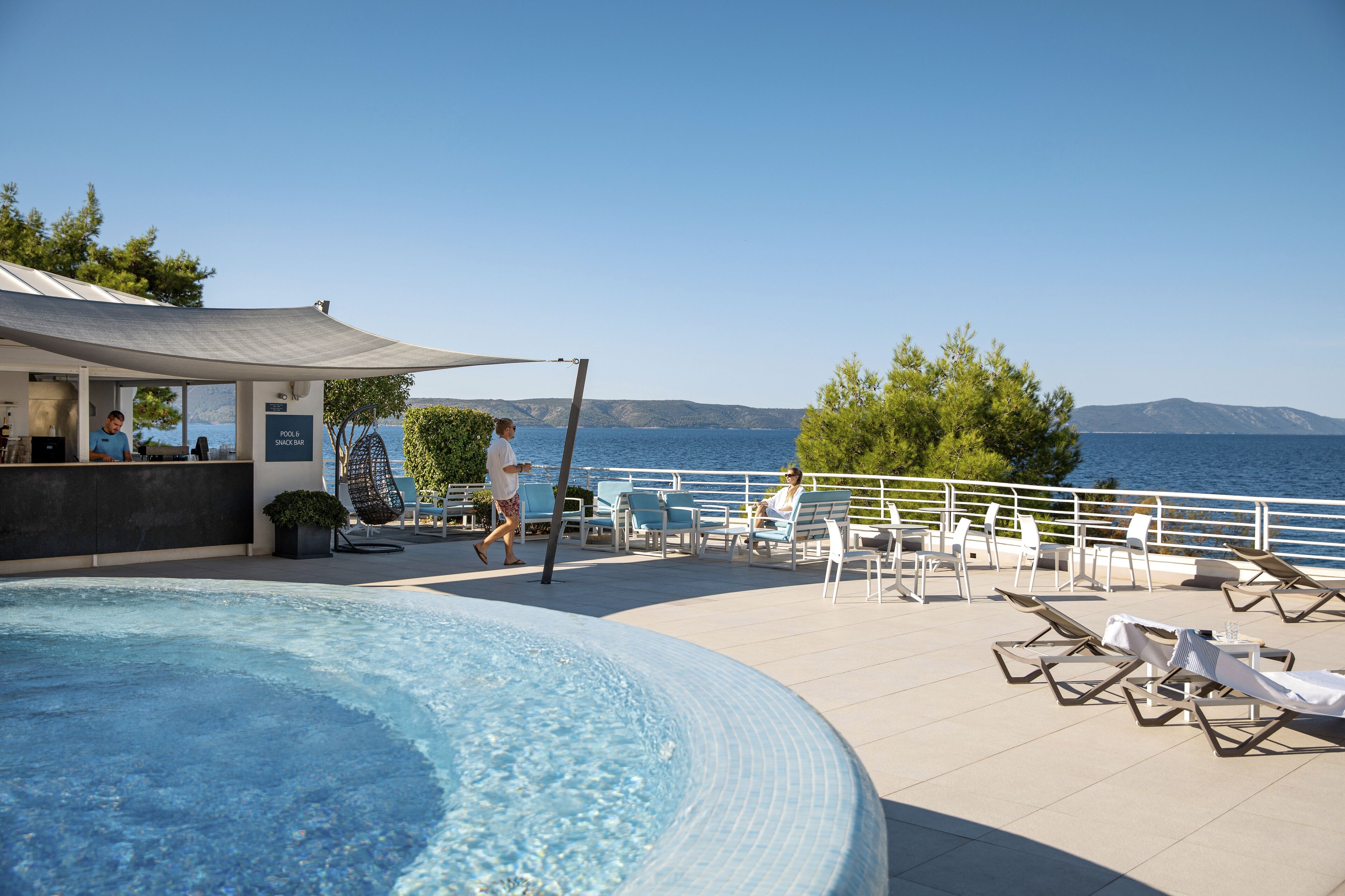 A pool area with lounge chairs and a bar, overlooking a body of water.