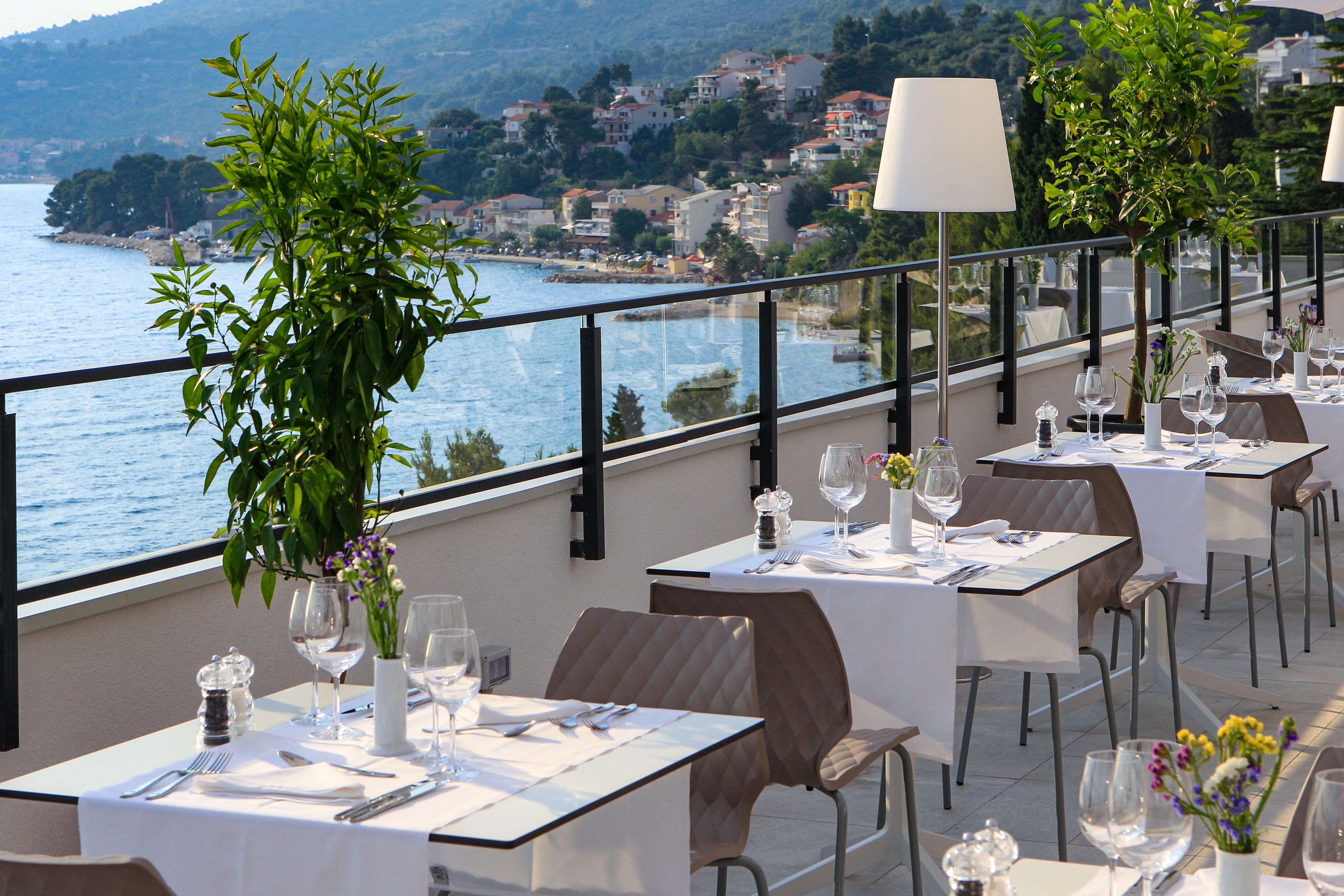 A terrace with tables set for dining, overlooking a coastal town.