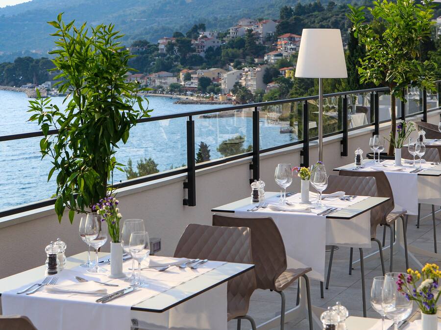 A terrace with tables set for dining, overlooking a coastal town.