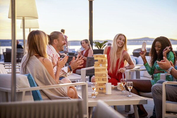 A group of people playing a board game at an outdoor table with a view of the sea. - TUI BLUE Adriatic Beach - Adults Only - All Inclusive (Podgora)