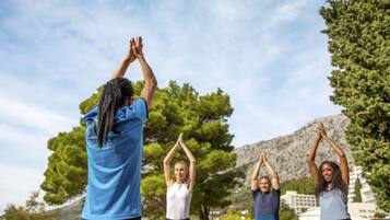 A group of people performing yoga outdoors with trees and a mountain in the background.