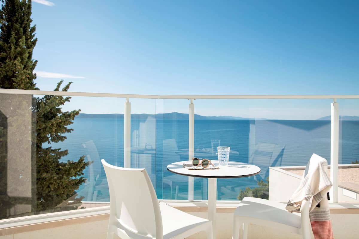 A balcony with a table and chairs, overlooking a scenic view of the sea and mountains.
