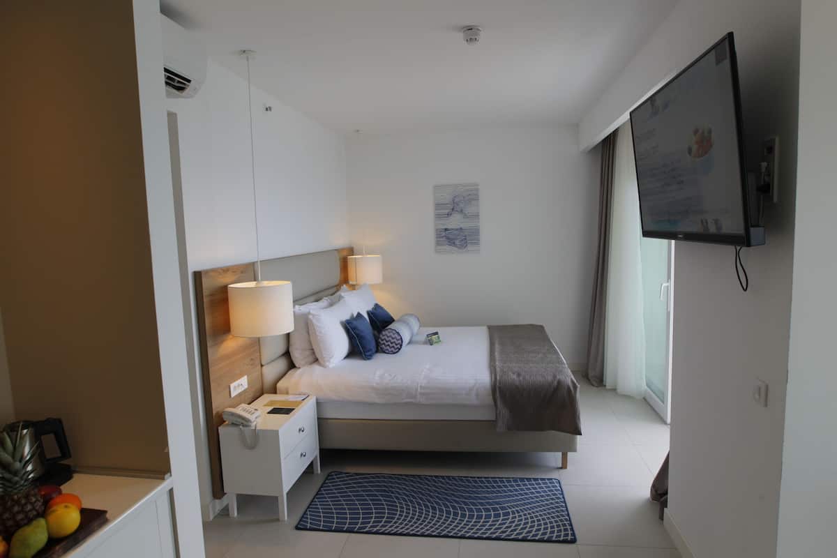 A modern hotel room with a bed, bedside lamps, a flat-screen TV, a small bedside table, and a fruit bowl.