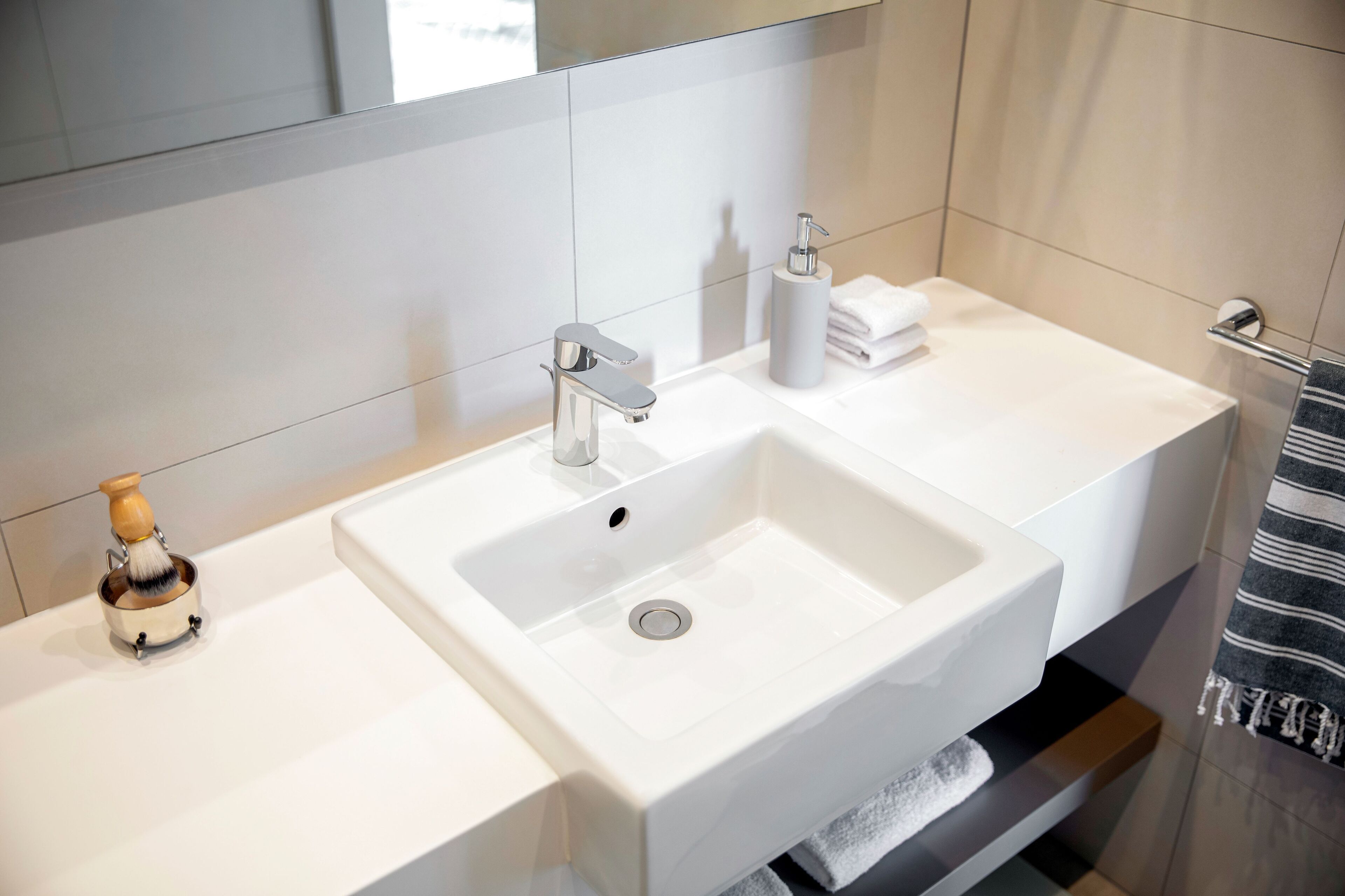 A modern bathroom with a white sink, chrome faucet, and a soap dispenser.