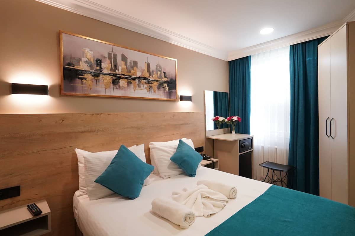 Ein Hotelzimmer mit einem großen Bett, einem Bild an der Wand, einem Schreibtisch mit Spiegel und einem Kleiderschrank.