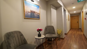 A hotel hallway with a wooden floor, two armchairs, a small table with a vase of flowers, and a painting of a cityscape on the wall. - The Marist Hotel Kadikoy (Istanbul)
