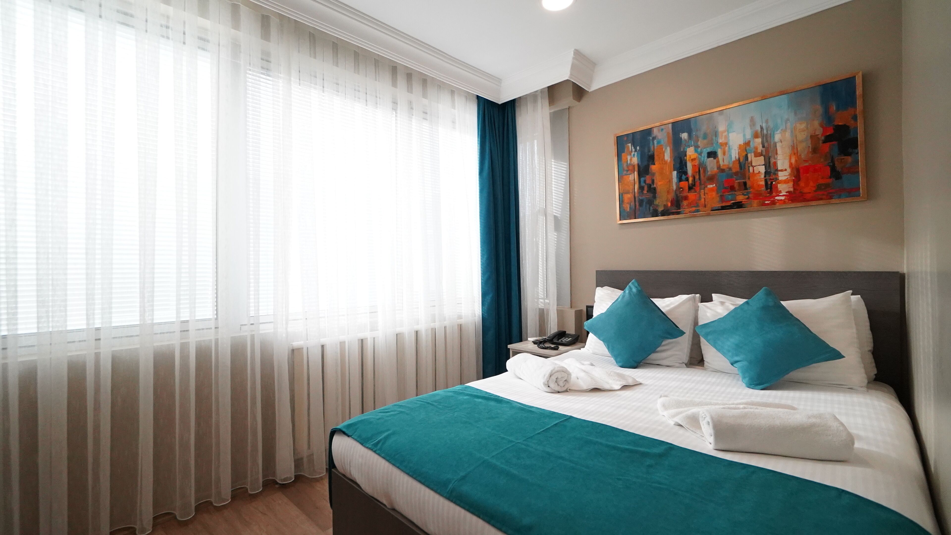 Une chambre d’hôtel avec un lit, un tableau au mur et une fenêtre ornée de rideaux légers.