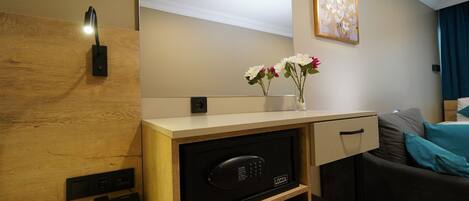 Una habitación de hotel moderna con un escritorio de madera, microondas integrado, teléfono y un florero con flores.