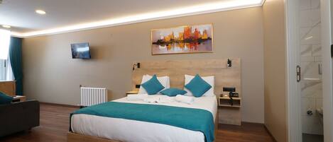 Una habitación de hotel moderna con una cama de madera, ropa de cama color turquesa, un televisor de pantalla plana, un cuadro y una mesita de noche con un teléfono.