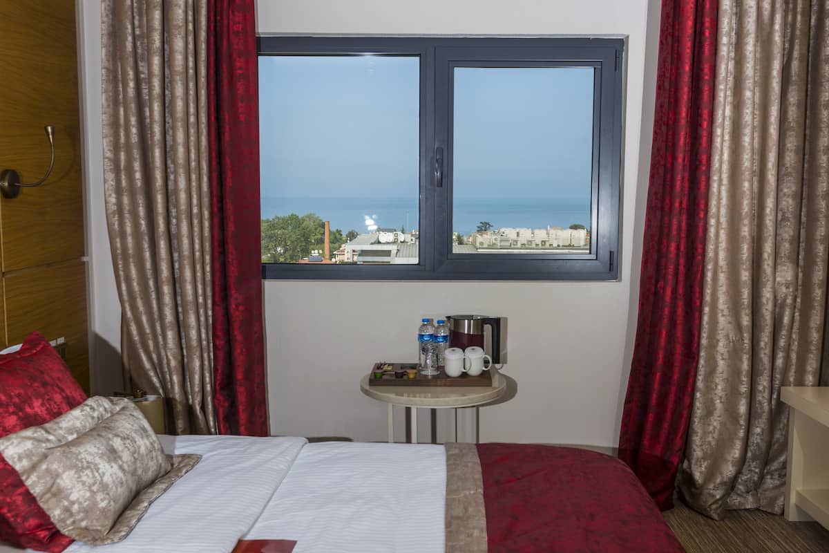 Een hotelkamer met een bed, een klein tafeltje met voorzieningen en een raam met uitzicht op zee en gebouwen.