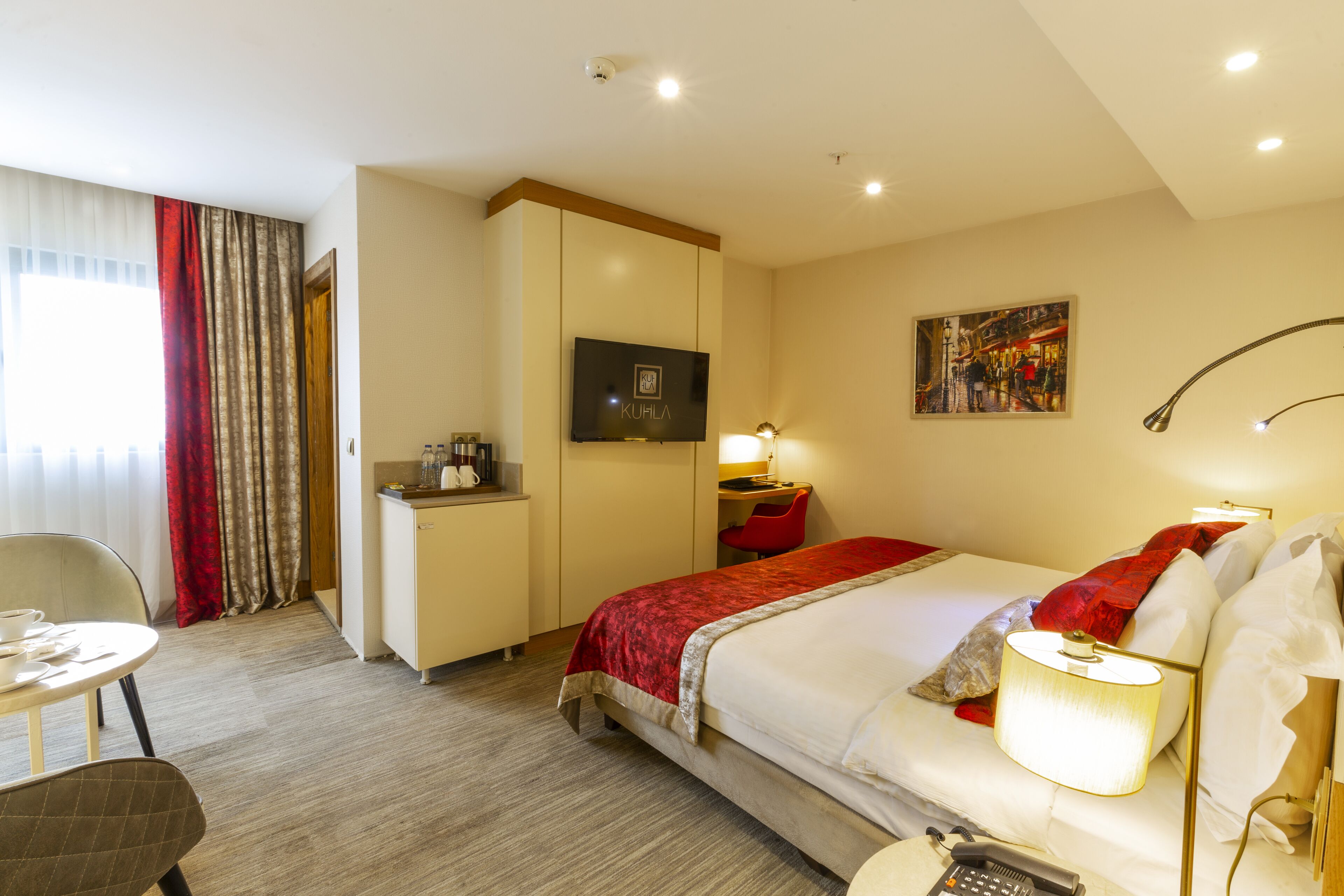A hotel room with a bed, a desk, a chair, a TV, and a painting on the wall.