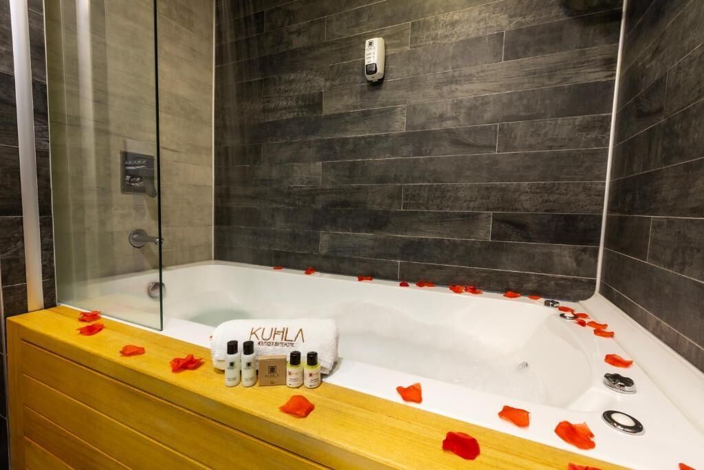 A modern bathroom with a bathtub, rose petals, and a towel with 'KUHLA' branding.