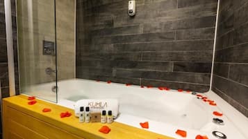 A modern bathroom with a bathtub, rose petals, and a towel with 'KUHLA' branding.