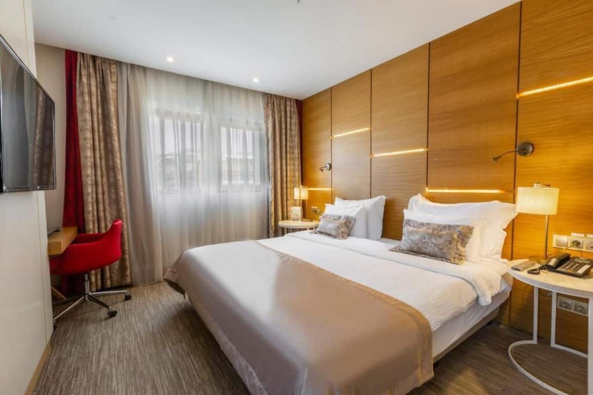 Een hotelkamer met een groot bed, twee nachtkastjes met lampen, een bureau met stoel, en een aan de muur bevestigde televisie.