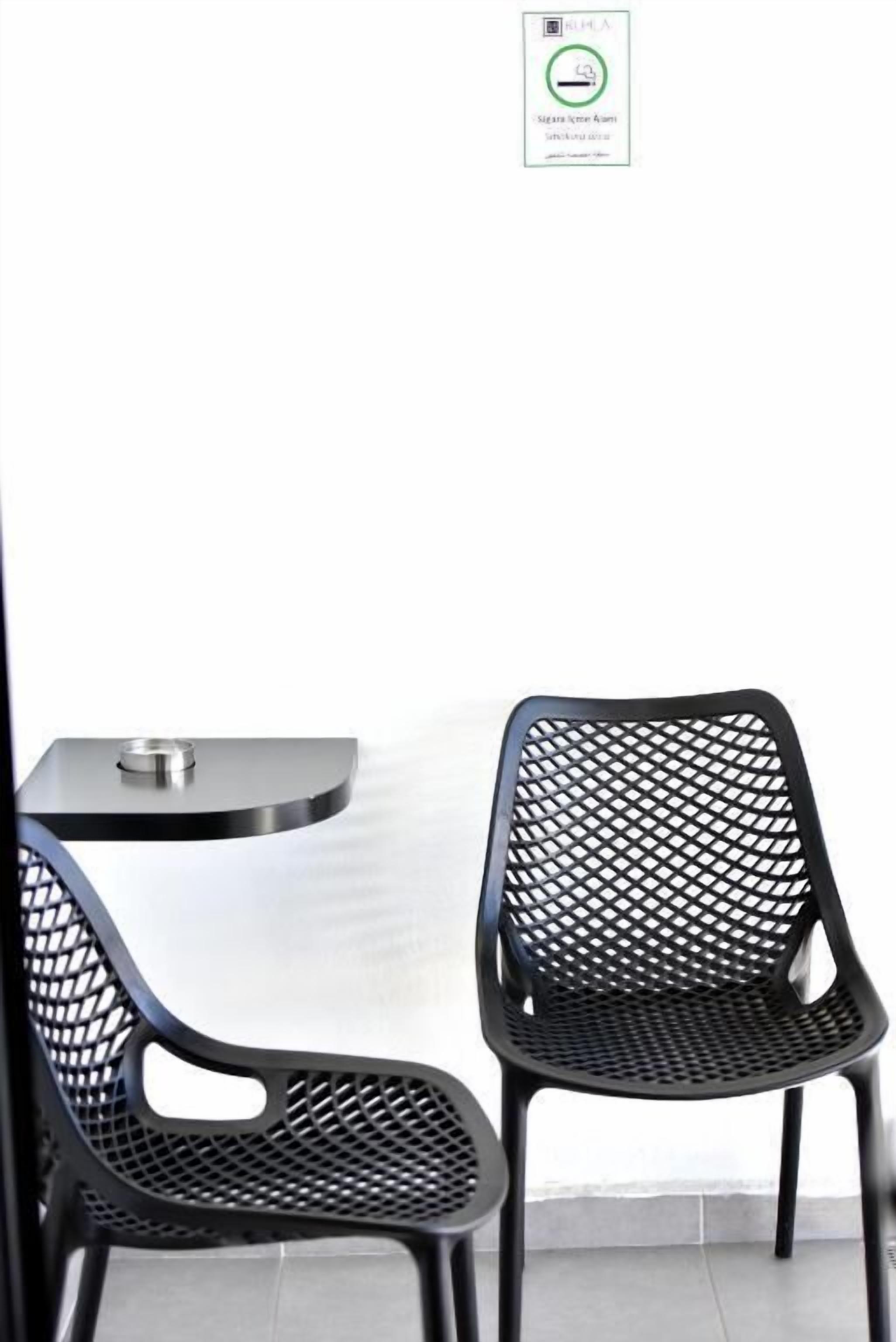 Two black mesh chairs and a small table in a room with a white wall and a window.
