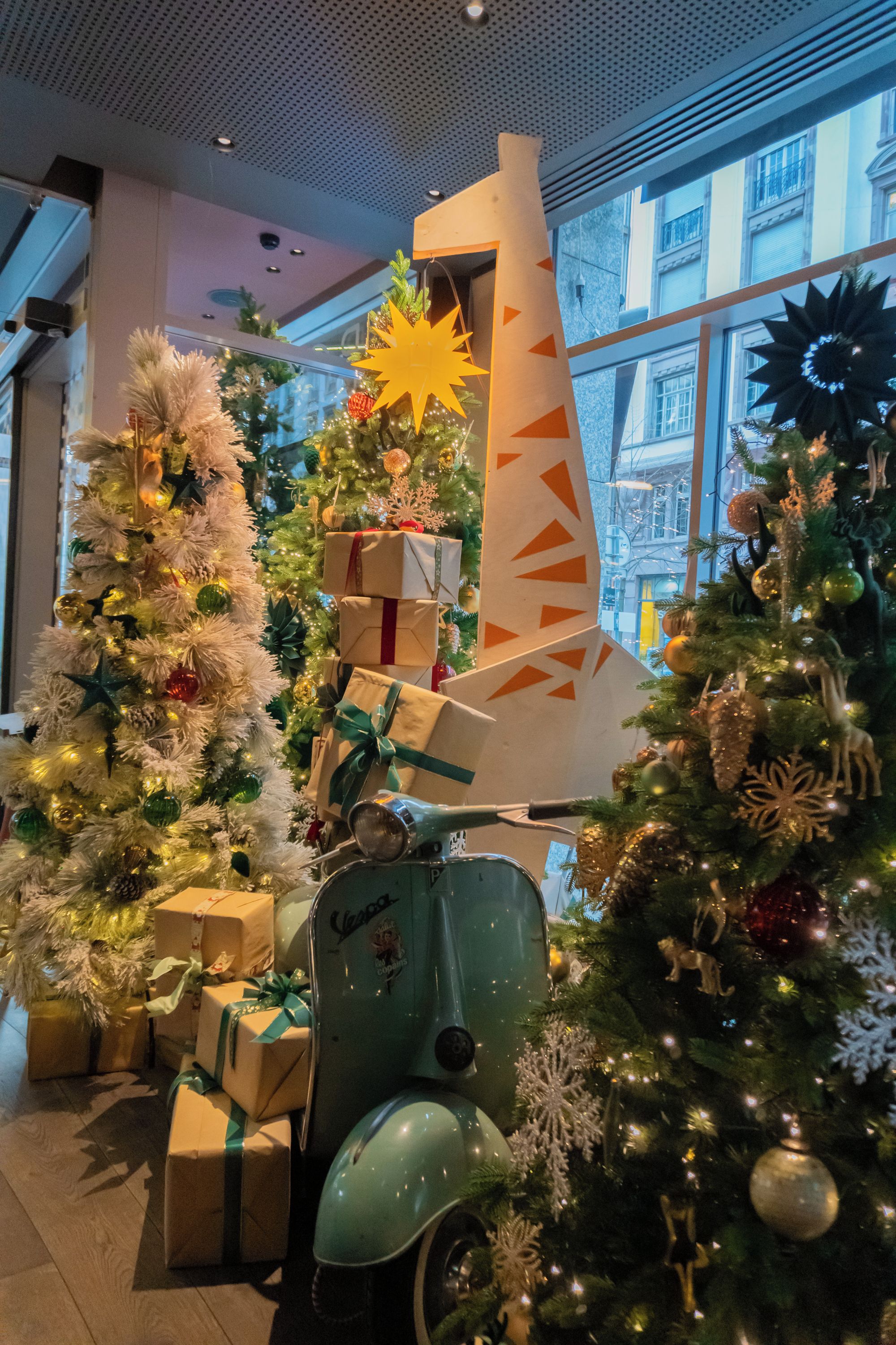 A Christmas display with decorated trees, gift boxes, and a vintage scooter.