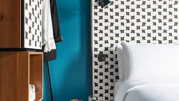 A bedroom with a wooden wardrobe, a bed with a patterned headboard, and a small round table with a book and a glass.